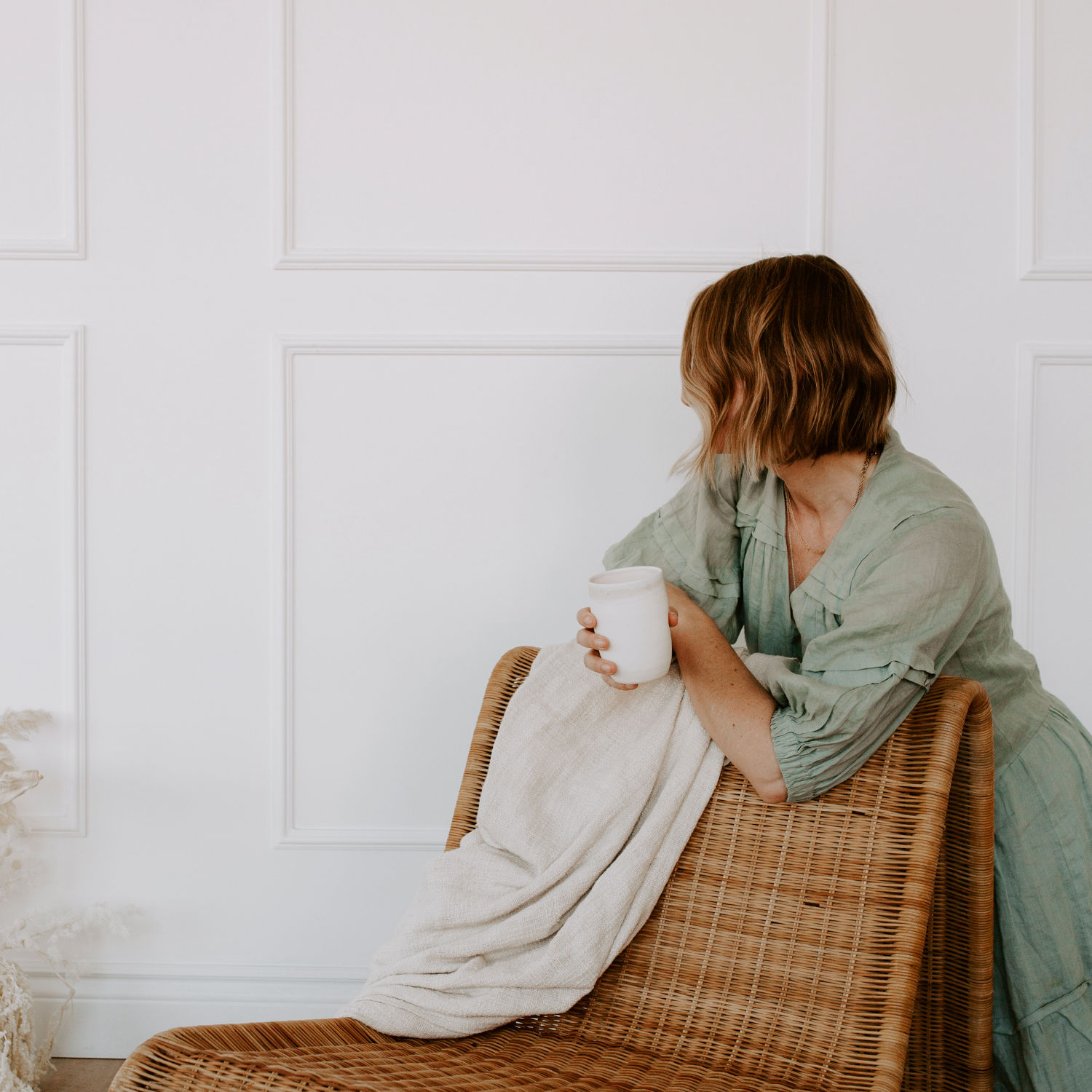 Woman in a white shirt holding a mug by the window, symbolising calm and improved wellbeing through hormone health support