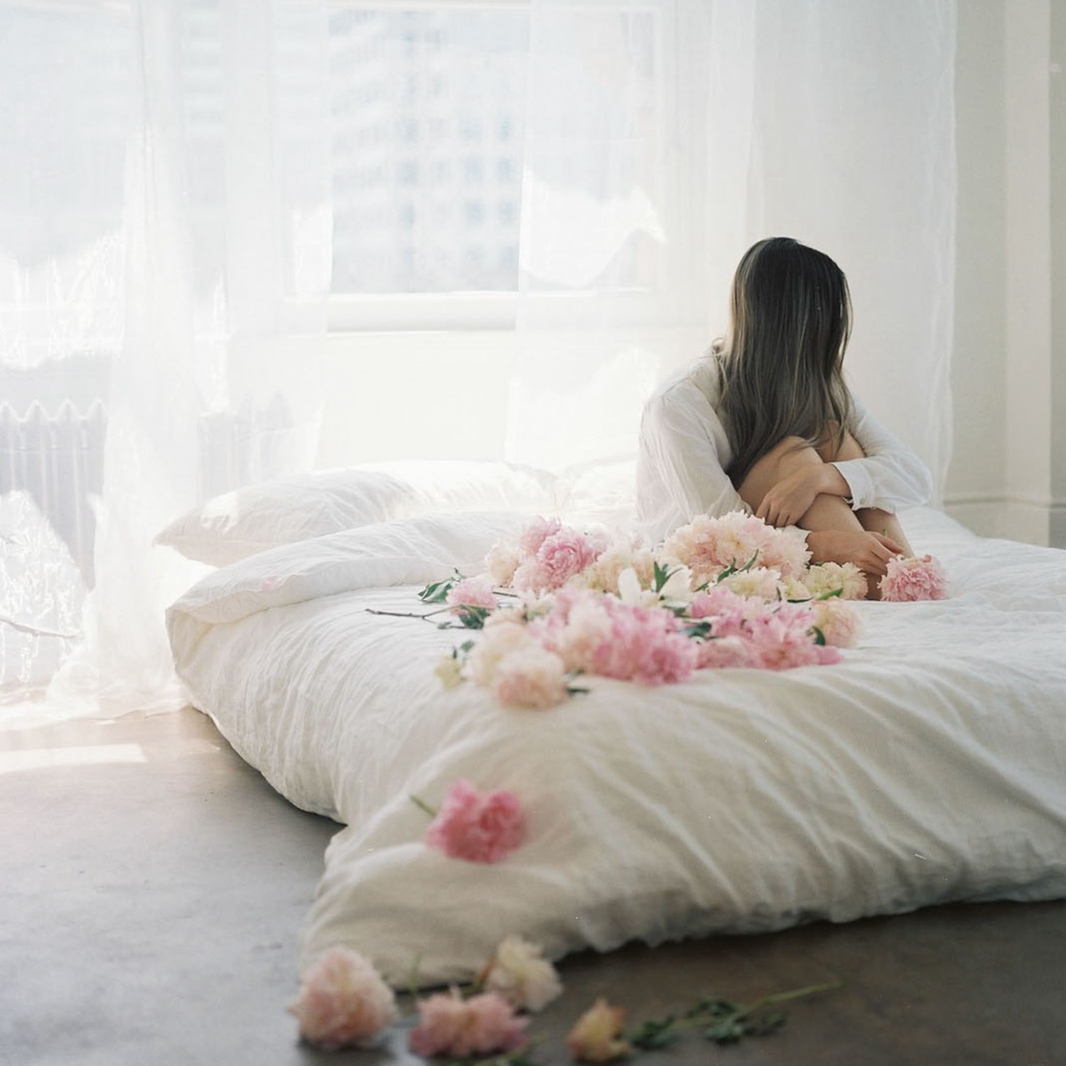 Woman in a white shirt holding a mug by the window, symbolising calm and improved wellbeing through hormone health support