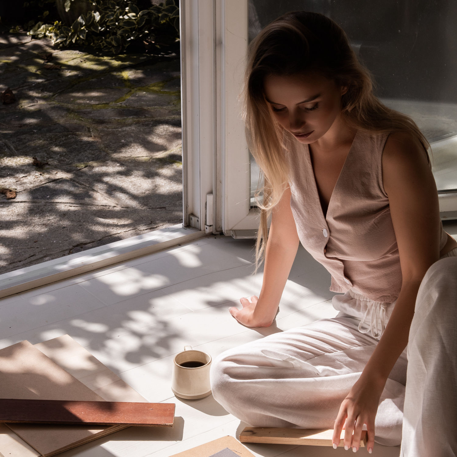 Woman in a white shirt holding a mug by the window, symbolising calm and improved wellbeing through hormone health support